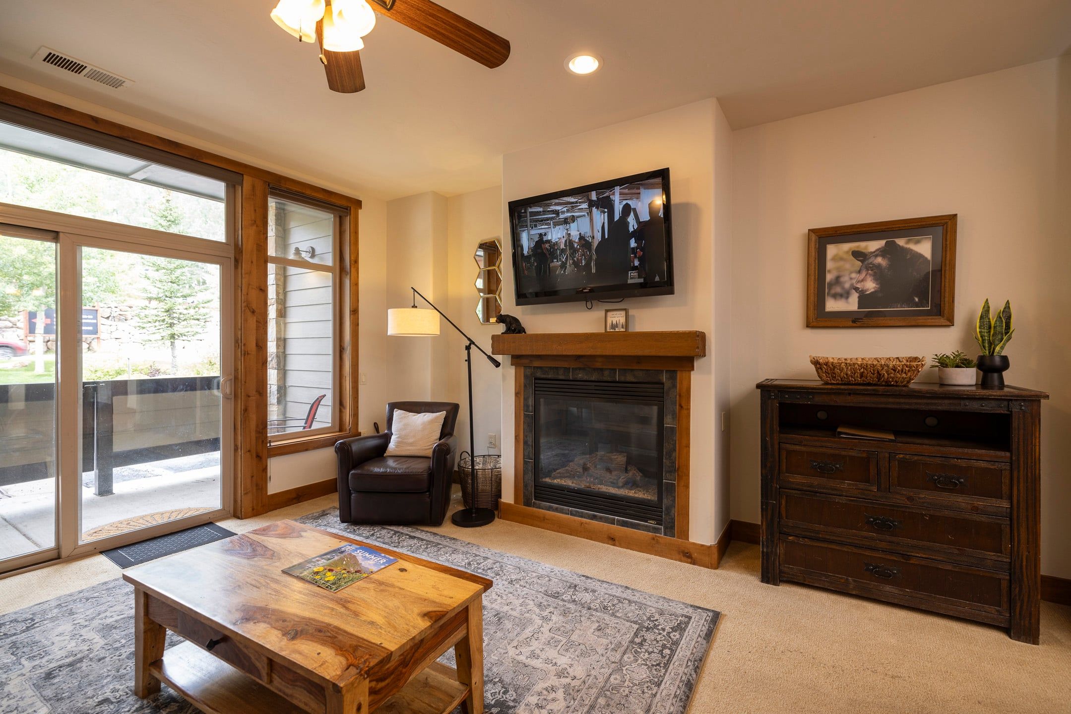 A cozy living room with a fireplace, a television mounted above it, and a comfortable seating area with a leather sofa and a wooden coffee table.