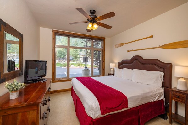 A hotel room with a bed, a television, a window, and a ceiling fan.