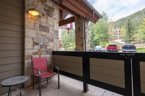 A stone exterior wall with a red chair and a small table, a black metal fence, and a view of parked cars and buildings in the background. - Experience comfort and adventure at Peregrine Point 103, a spacious 2-bedroom condo (Durango)