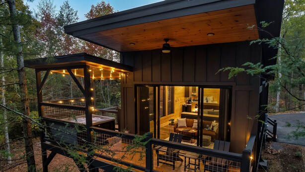 Una cabaña con terraza, zona de estar exterior cubierta y un interior acogedor con sofá y mesa.