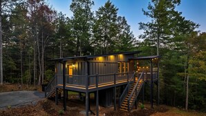 Una cabaña moderna con terraza de madera, escaleras y porche cubierto.