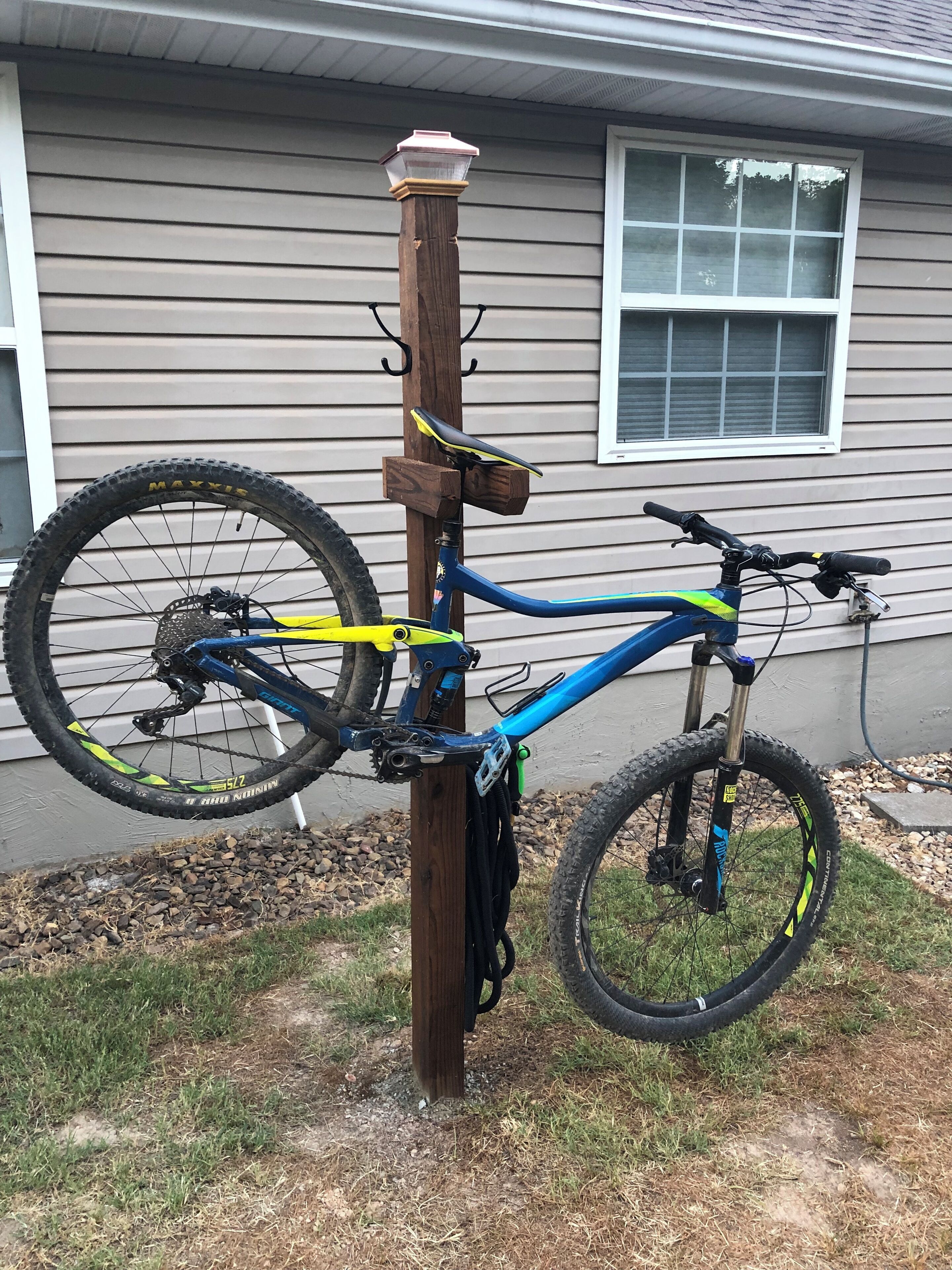 Una bicicleta de montaña azul estacionada junto a un poste de madera frente a una casa.