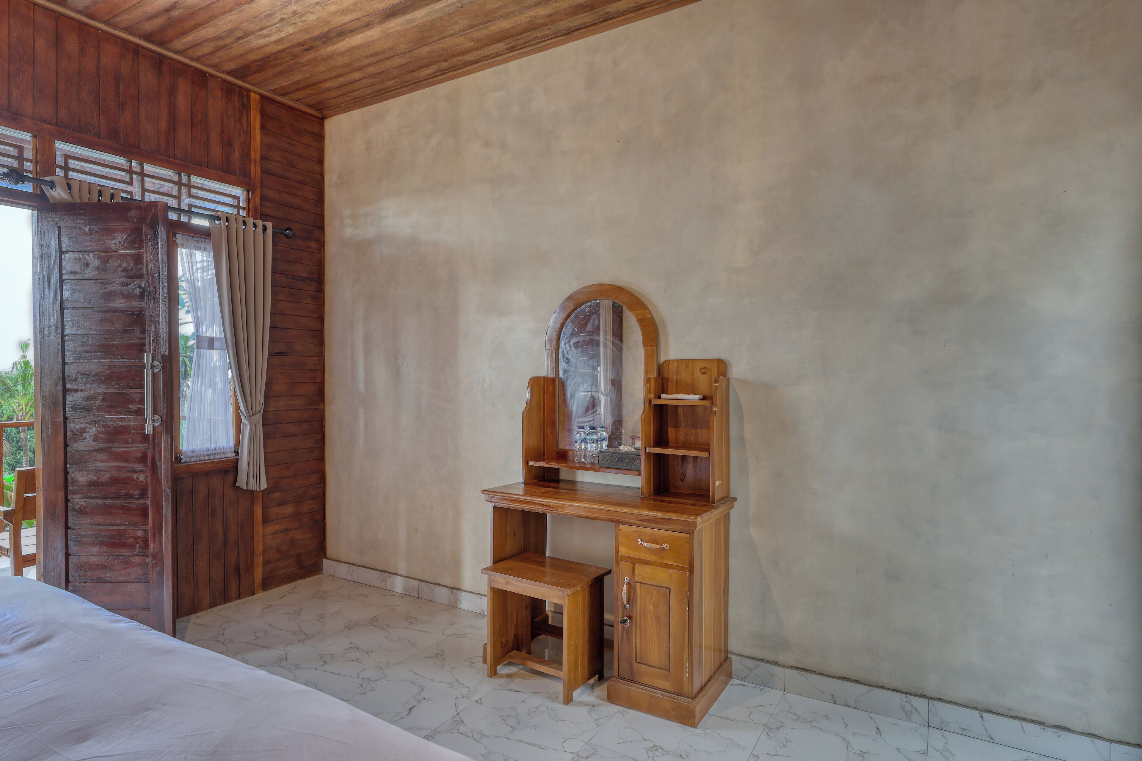A wooden desk with a mirror, a small bench, and a cabinet in a room with a wooden door and a view outside.