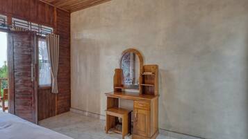 A wooden desk with a mirror, a small bench, and a cabinet in a room with a wooden door and a view outside.