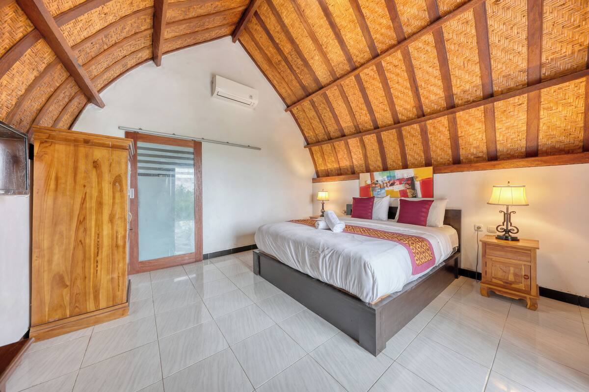 A bedroom with a large bed, a wooden wardrobe, a glass door, and a ceiling with a woven pattern.