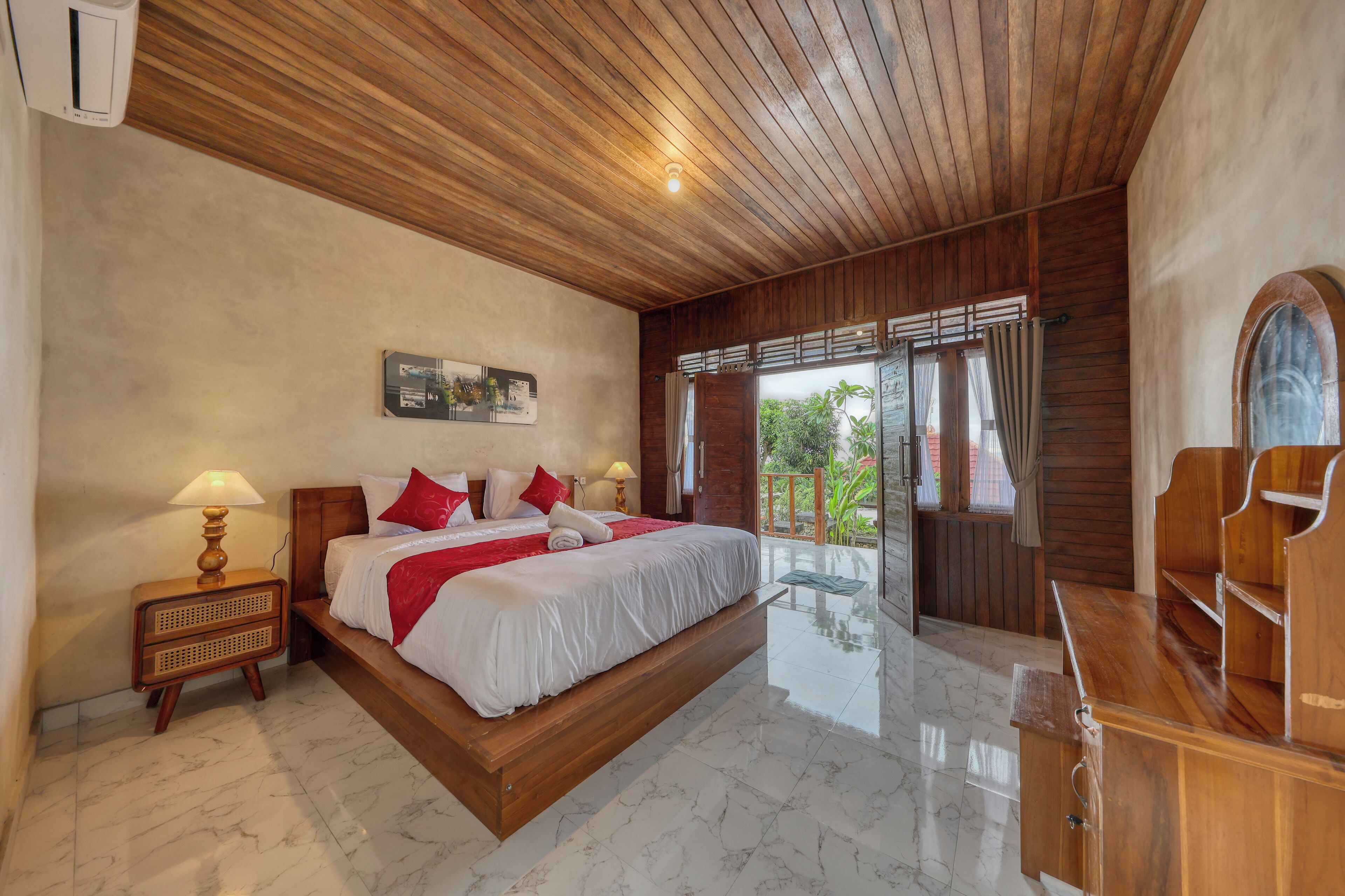 A bedroom with a large bed, wooden ceiling, and a balcony with a view.