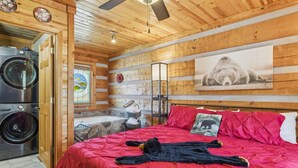 A cozy room with a large bed, a washing machine, a bathtub, and a wooden ceiling. - Lovey Bear - A Cozy Dog-Friendly Cabin with Hot Tub, Fireplace – Across from Soaky Mountain (Sevierville)