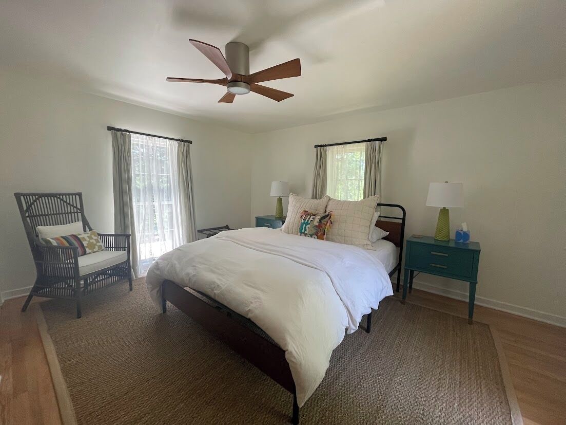 A bedroom with a bed, a chair, a nightstand, a lamp, and a ceiling fan.