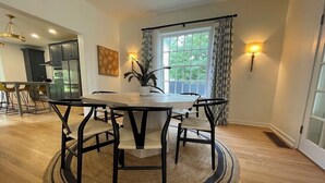Un comedor con una mesa redonda y sillas, una planta en maceta y vistas de la cocina y el exterior a través de una ventana.