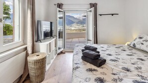 Un dormitorio con cama, televisión, vistas a montañas y un balcón.