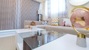 Una sala de estar moderna con una mesa de centro de vidrio, un sofá color beige con cojines estampados y un globo decorativo sobre un pedestal.