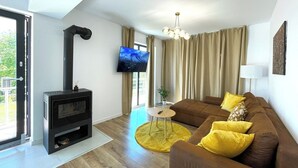 A modern living room with a fireplace, a sofa, a TV, and a large window. - Nicme Villa Bran: Game Room and Barbecue (Bran)