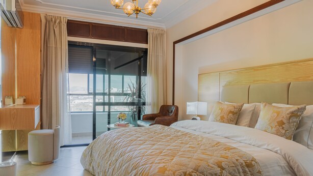 Una camera d'albergo con un letto grande, una sedia, una scrivania e vista sulla città attraverso un'ampia finestra.