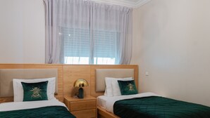 Una camera da letto con due letti, una testiera in legno, un comodino con una lampada e una finestra con tende leggere.