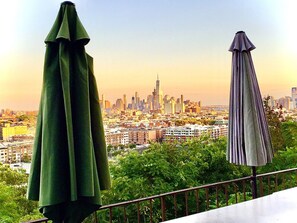 A balcony with two umbrellas overlooking a cityscape with a prominent skyscraper.
