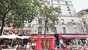 A café with outdoor seating, red umbrellas, and a banner advertising 'La Baguette du Relais'. - Quiet Studio for 2 People - Le Marais (Paris)