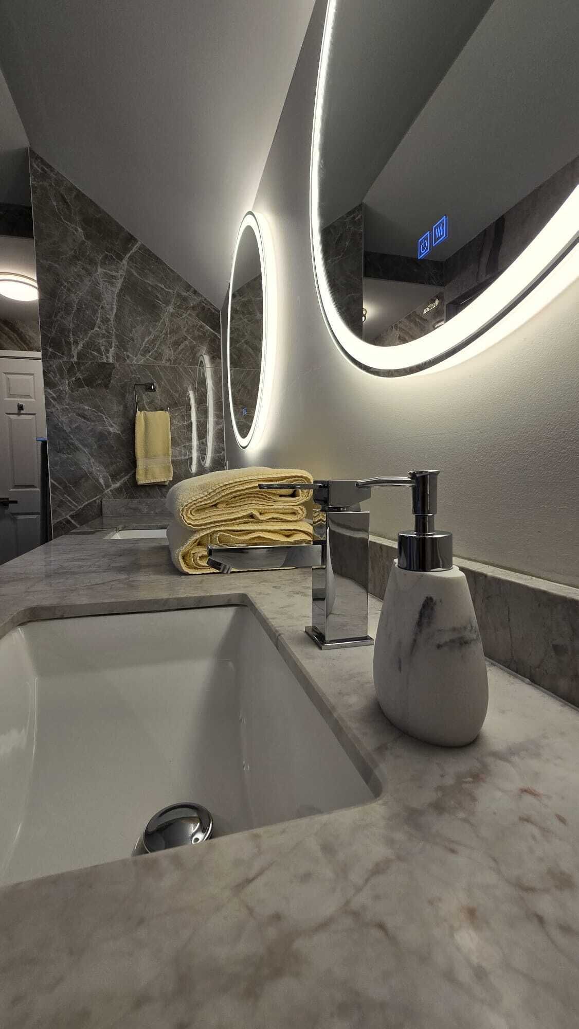 Une salle de bain moderne avec un grand lavabo, un porte-serviettes et un miroir doté d’un cadre éclairé.