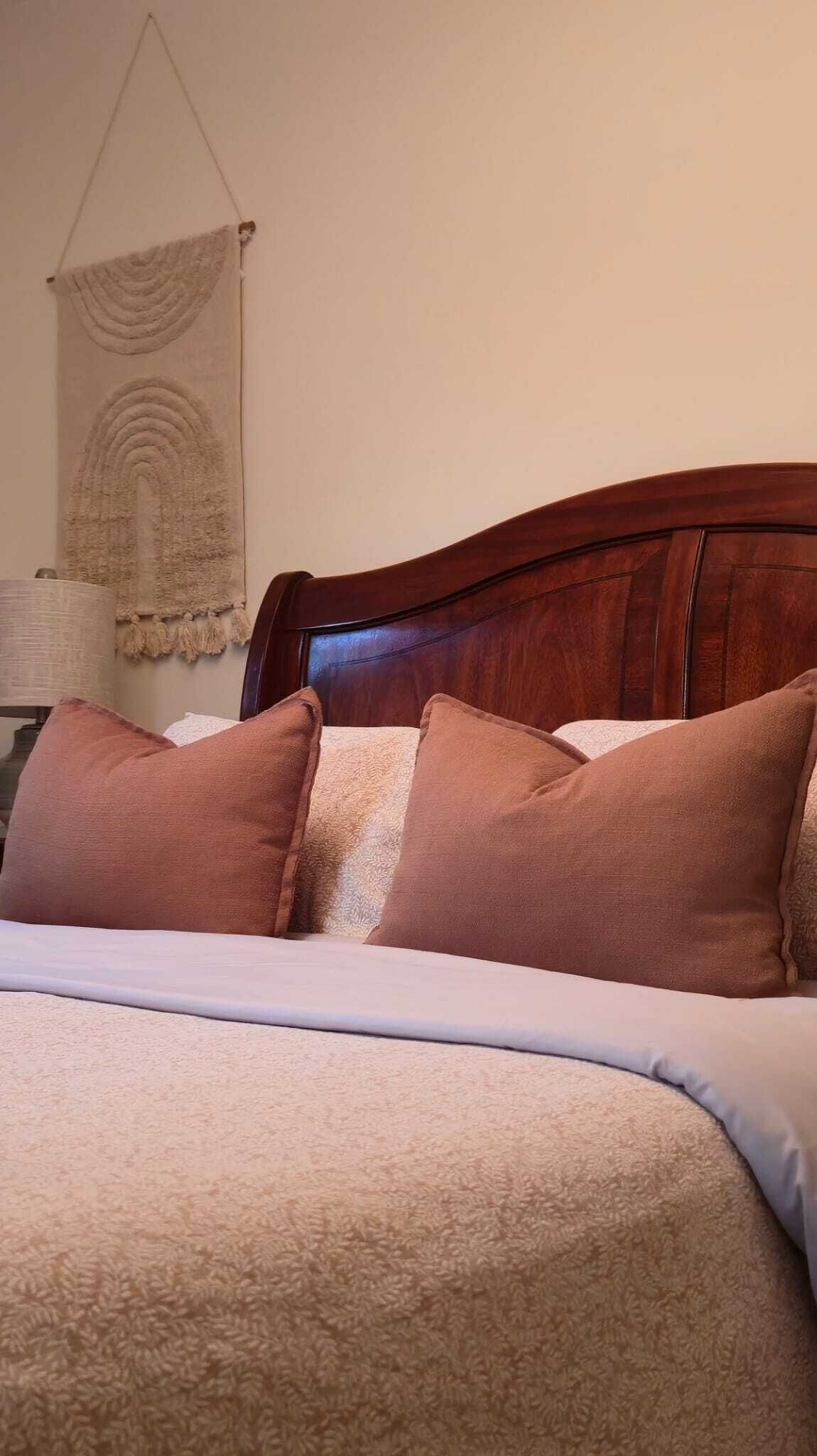 Un lit bien fait, avec une tête de lit en bois, plusieurs oreillers et une couverture à motifs.