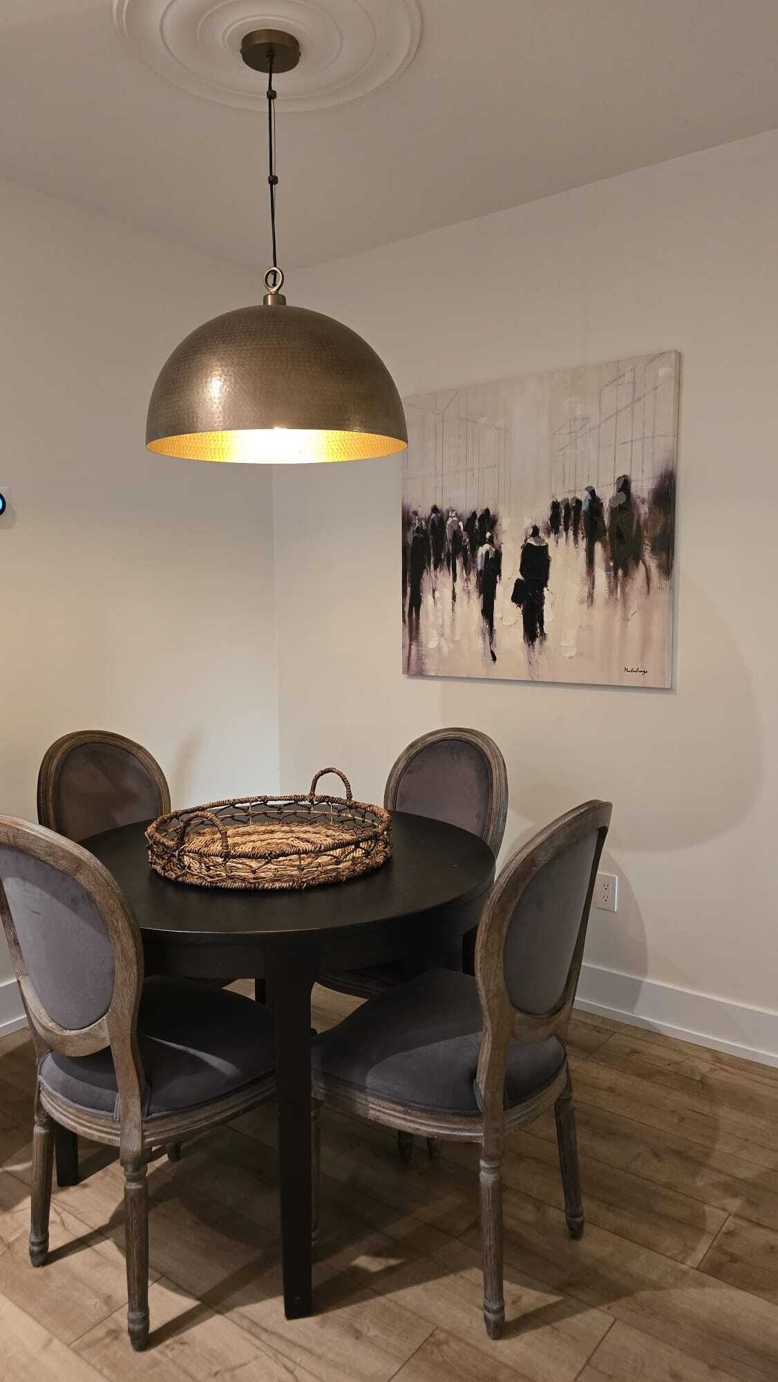Un coin repas comprenant une table ronde, quatre chaises, un panier en osier et une suspension.
