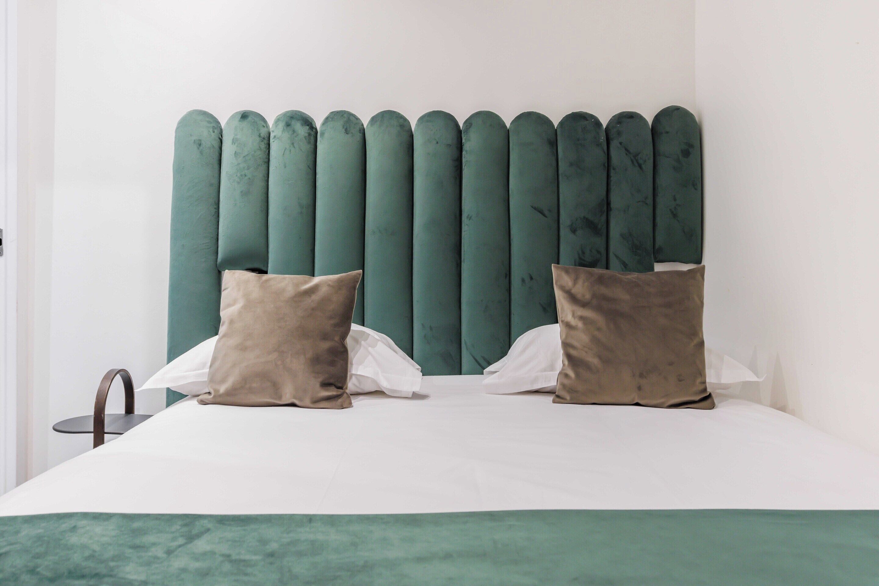 A bed with a teal upholstered headboard, two pillows, and a white bedspread.