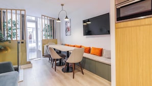 A modern kitchen with a dining area, wooden cabinets, a built-in oven, and a large flat-screen TV. - Charming Duplex - 2br/6p - In the Heart of Odeon (Paris)