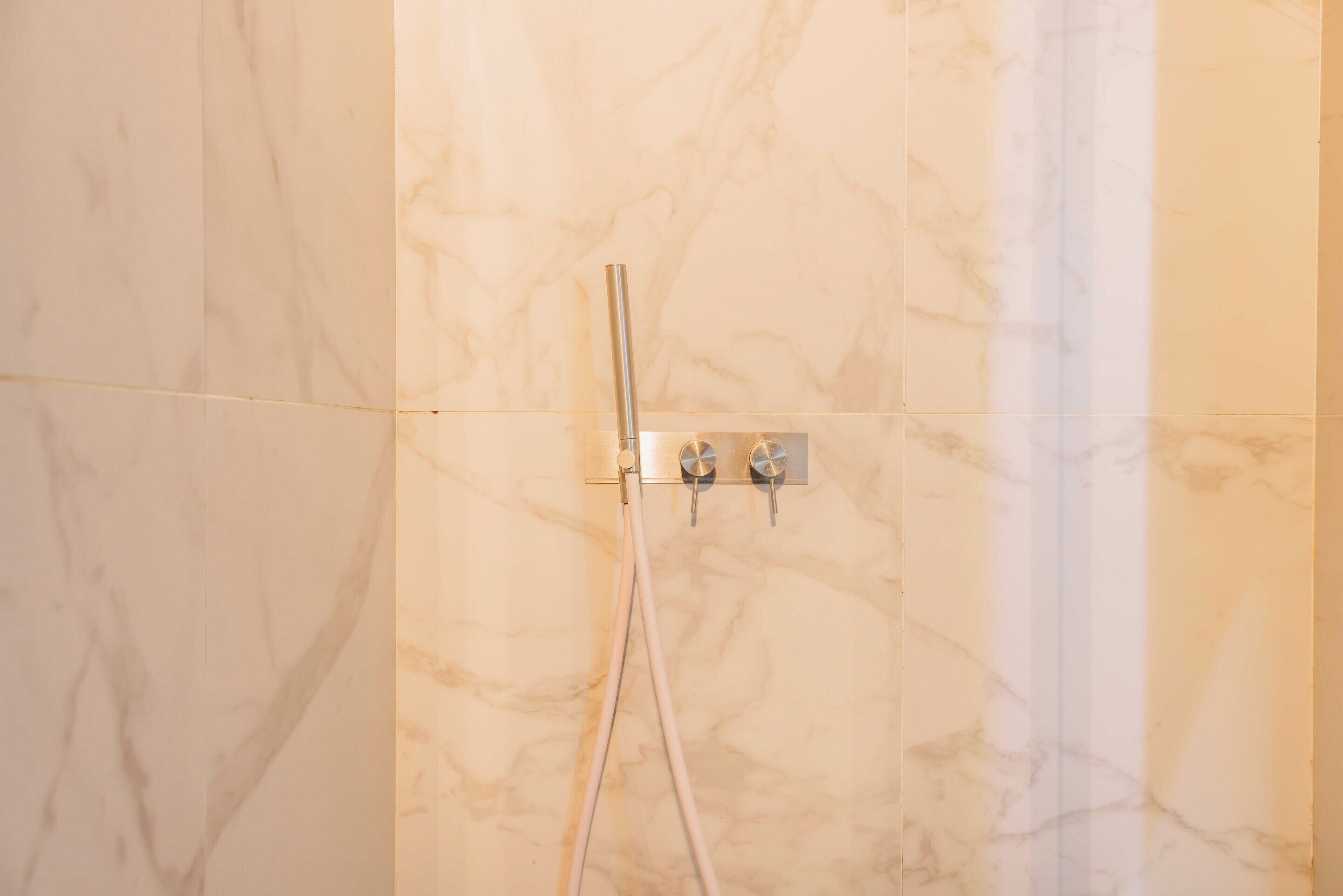 Ein Badezimmer mit Marmorwänden, einer Dusche inklusive Handbrause und zwei Wandarmaturen.