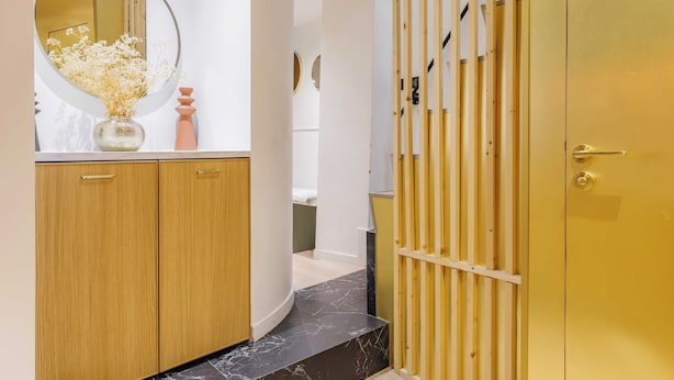 A hallway with wooden cabinets, a marble-tiled floor, a mirror with a vase of flowers, and a golden door. - Charming Duplex - 2br/6p - In the Heart of Odeon (Paris)