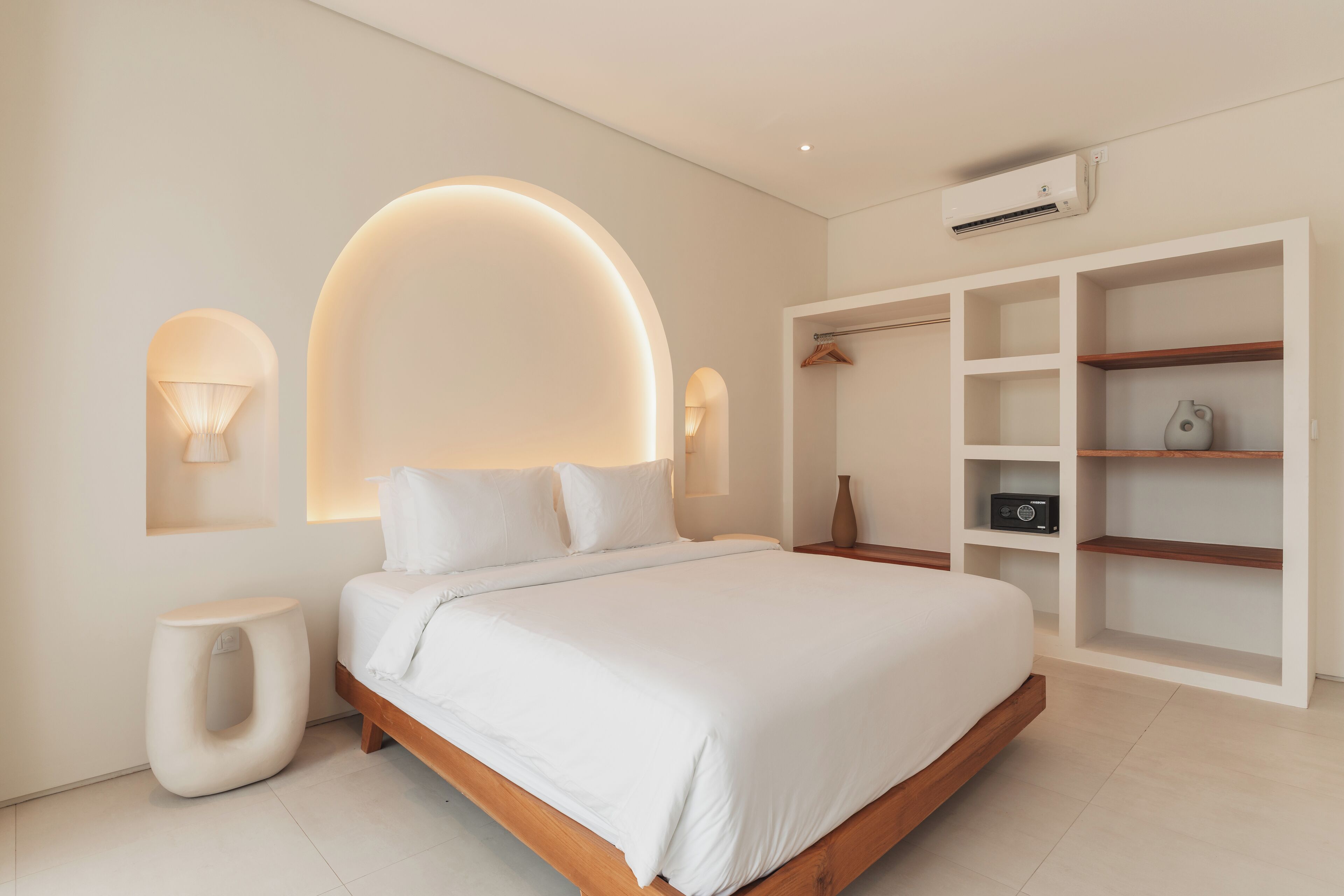A modern bedroom with a large bed, built-in shelving, and wall-mounted lighting.