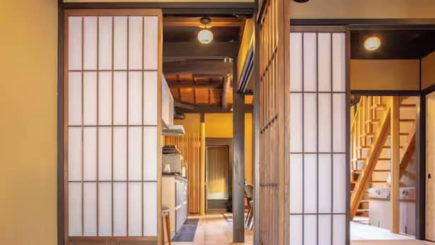 Ein traditionelles japanisches Interieur mit Schiebetüren, einer Holztreppe und einem Küchenbereich.