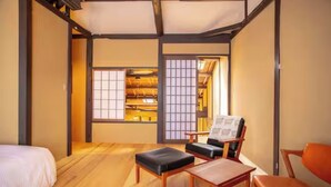 Ein traditioneller japanischer Raum mit Tatami-Böden, einem niedrigen Holztisch, einem gepolsterten Stuhl und einem Bett.