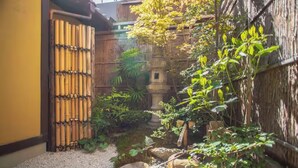 Ein Garten mit einem Bambuszaun, einem Kiesweg und verschiedenen Pflanzen.