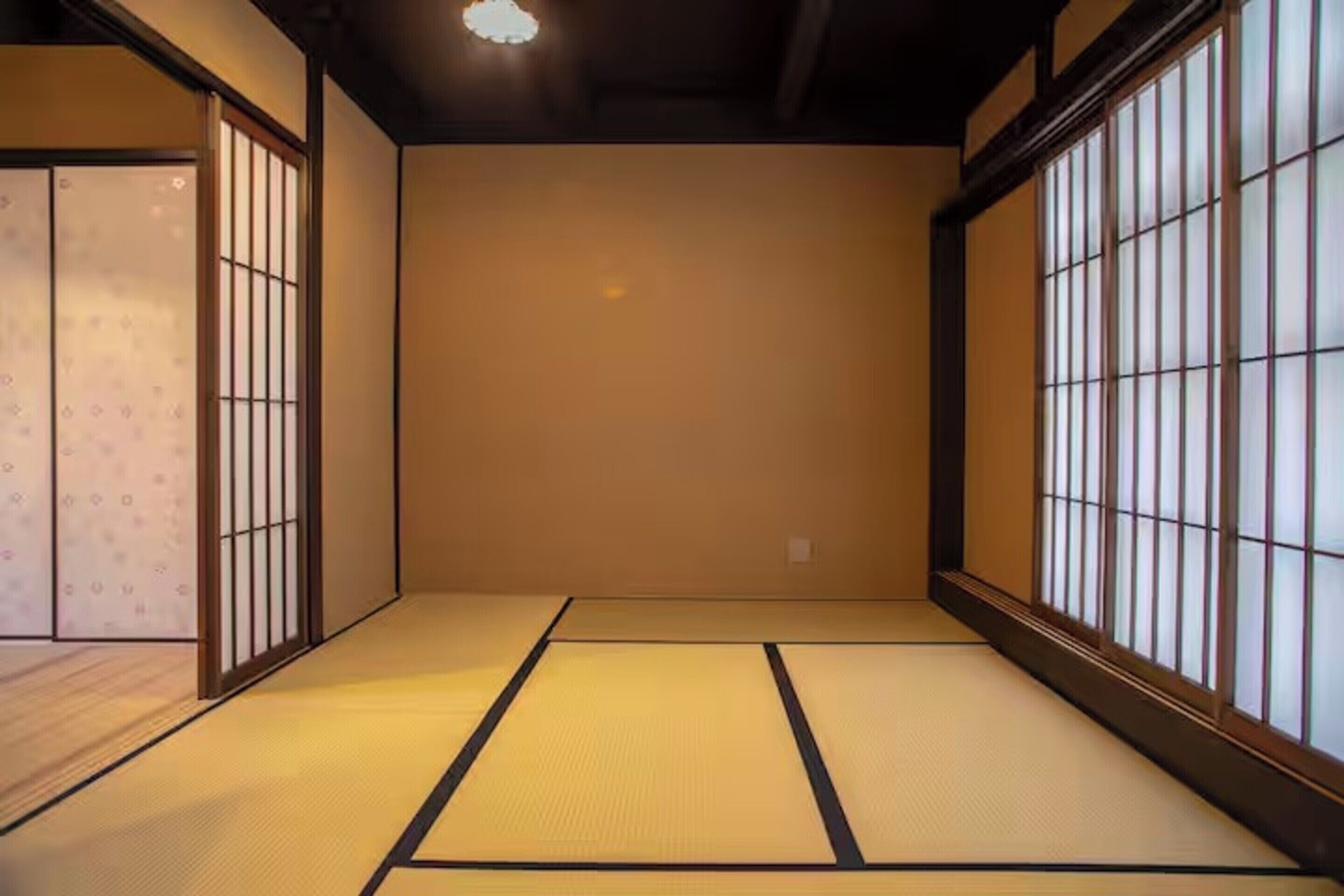 A traditional Japanese room with tatami flooring, sliding doors, and large windows with vertical blinds.