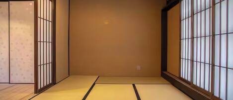 A traditional Japanese room with tatami flooring, sliding doors, and large windows with vertical blinds.