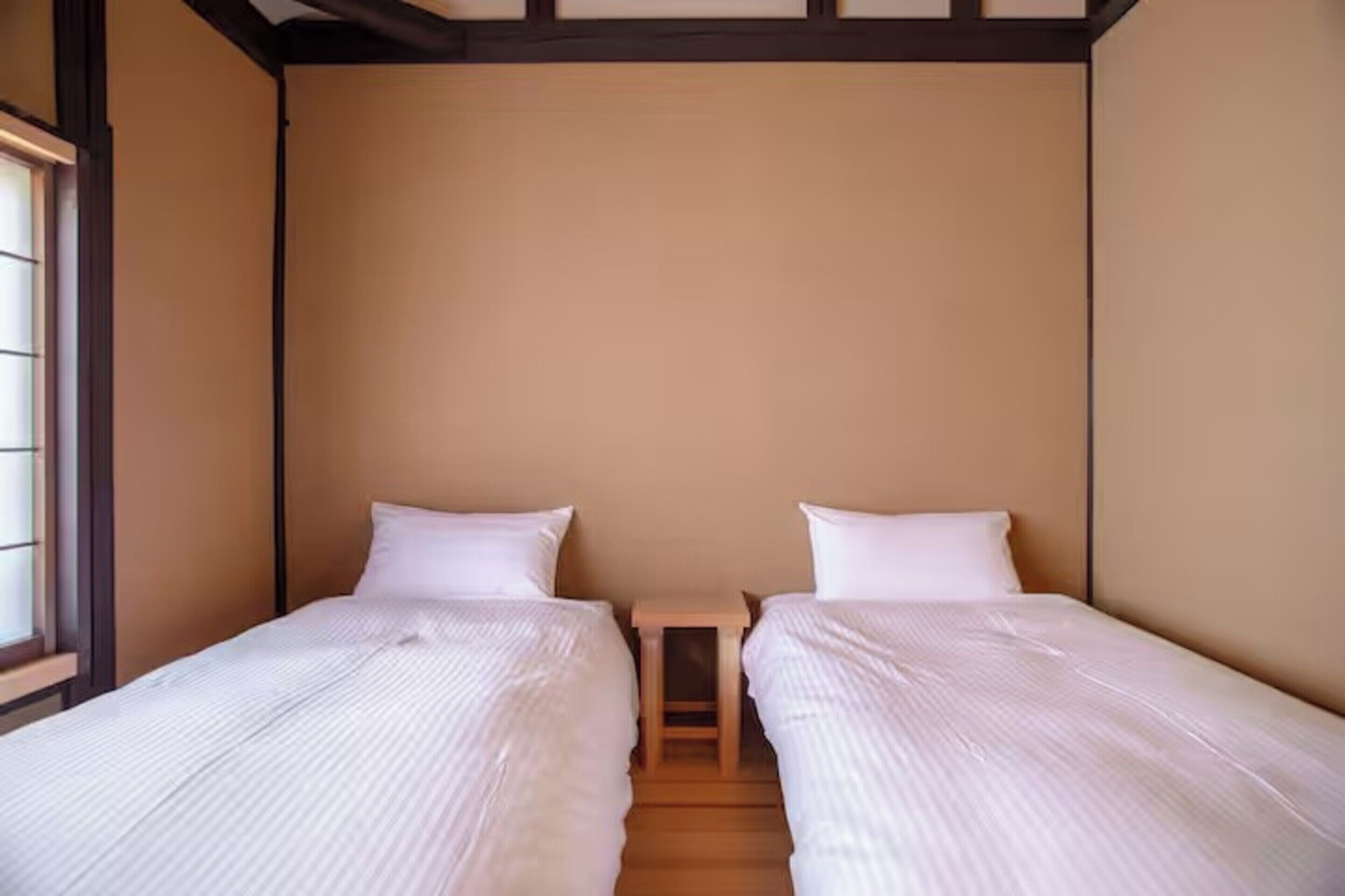 Una habitación con dos camas individuales, una mesita de noche de madera y una ventana a la izquierda.