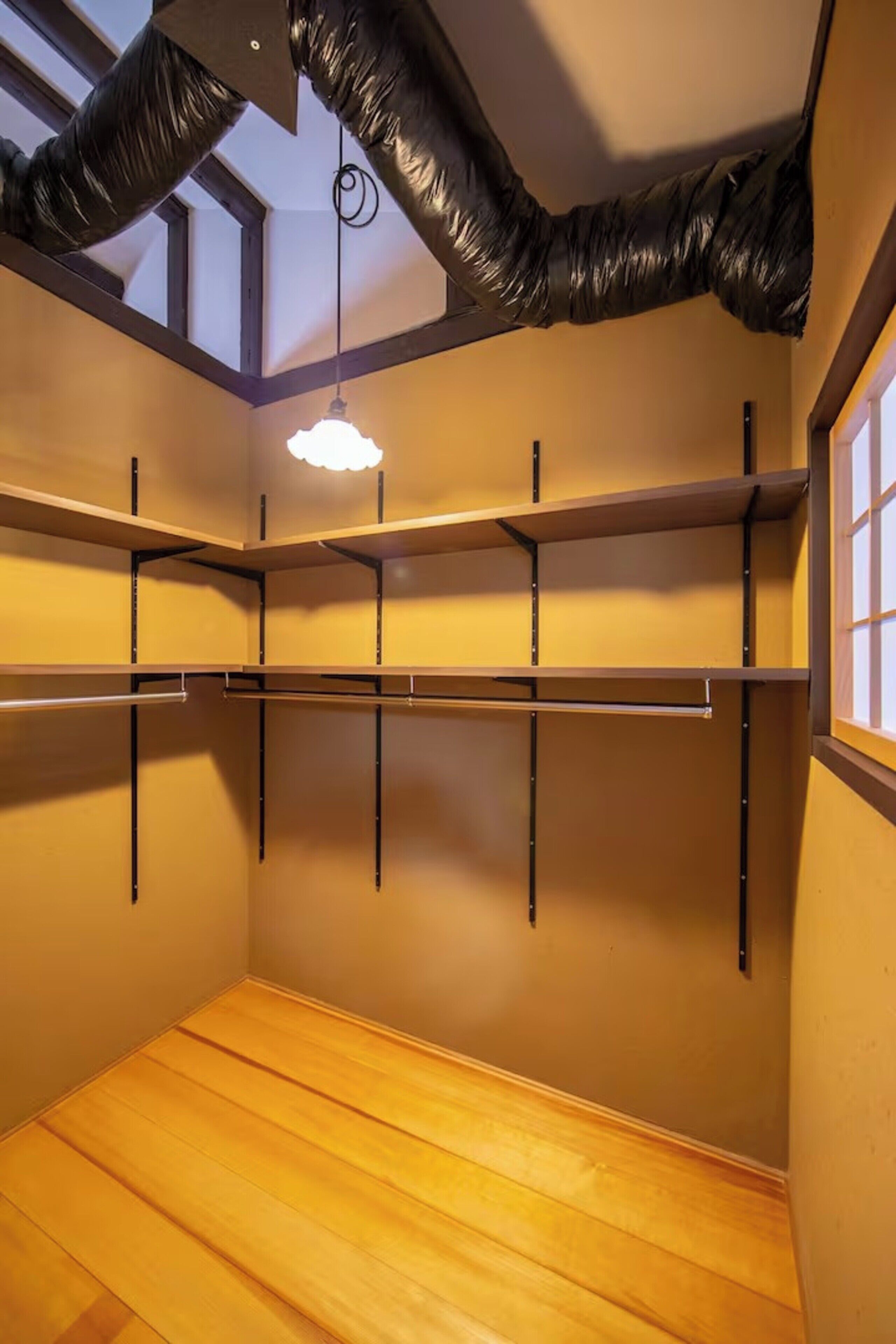 A room with wooden flooring, a slanted ceiling with black ductwork, and a single pendant light.