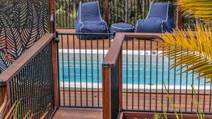 Una zona junto a la piscina con terraza de madera, dos sillones de relax y una piscina.
