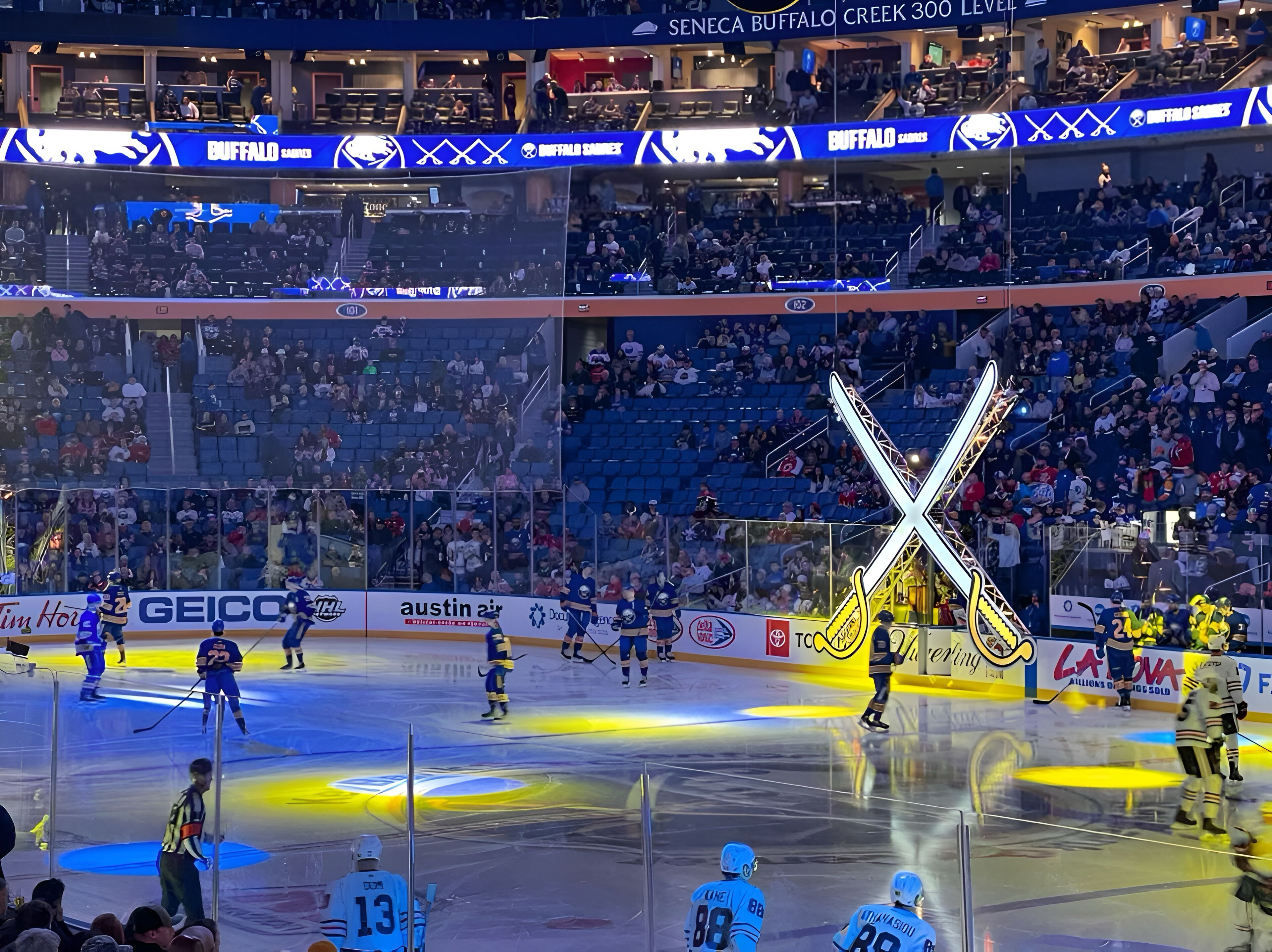 An indoor hockey rink with multiple levels of seating, advertisements, and a large illuminated X-shaped structure.