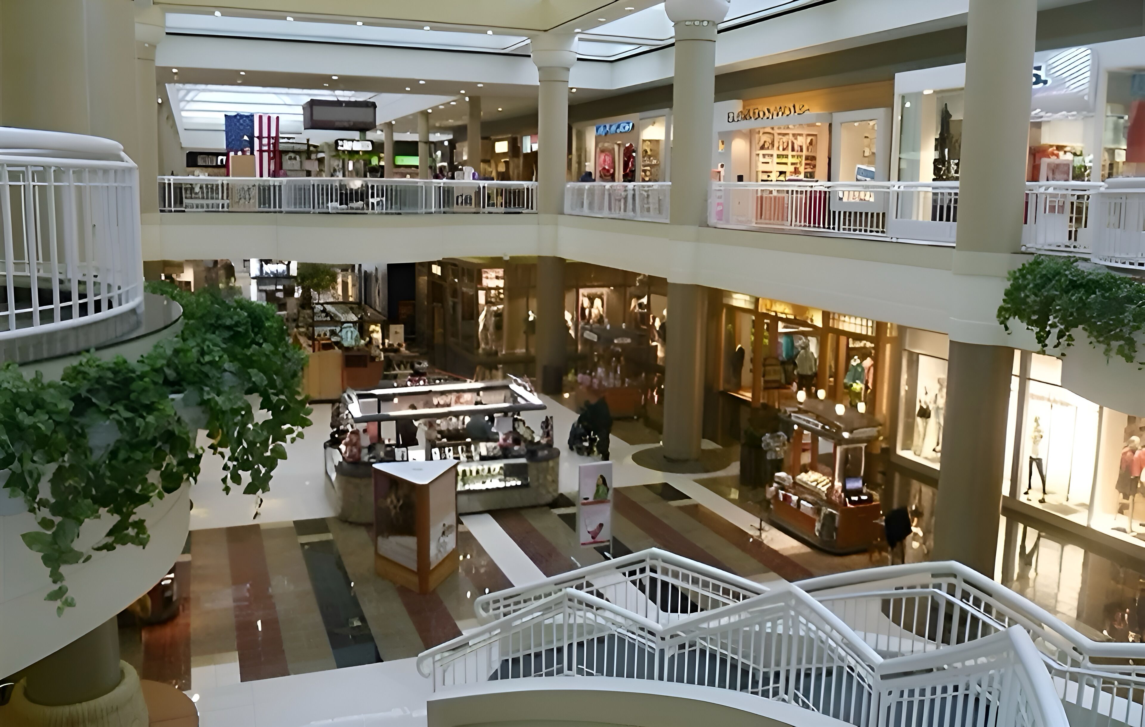 A multi-level shopping mall with various stores, a central kiosk, and a white railing.