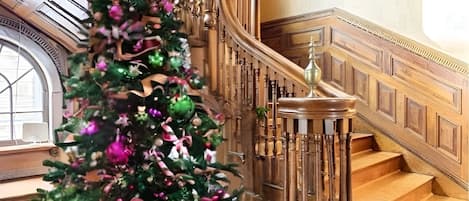 A grand staircase with a decorative railing and a Christmas tree adorned with ornaments and ribbons.