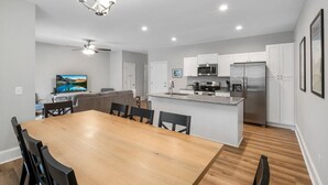 A modern kitchen with white cabinets, stainless steel appliances, and a wooden dining table with chairs. - Ducks Landing Accommodations at Southern Pines Golf Course (Aberdeen)