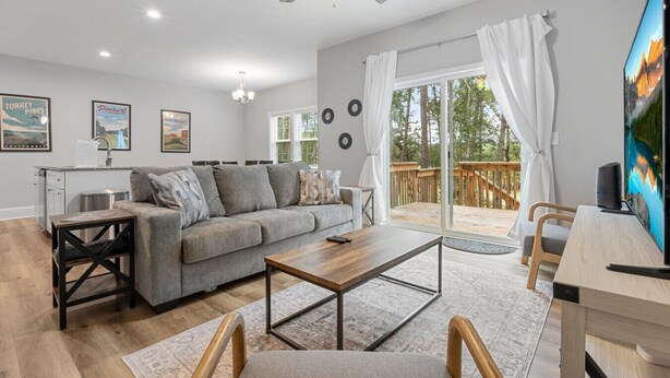 A spacious living room with a grey sofa, wooden coffee table, and a TV on a wooden stand. - Ducks Landing Accommodations at Southern Pines Golf Course (Aberdeen)