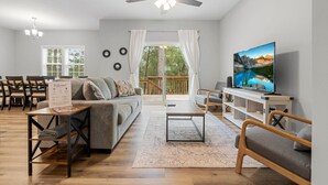 A spacious living room with a sofa, coffee table, and TV, a dining area with chairs, and a balcony with curtains. - Ducks Landing Accommodations at Southern Pines Golf Course (Aberdeen)