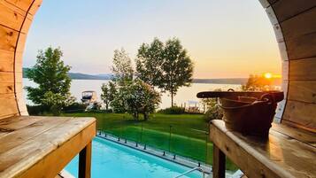 Enjoy the serene view of the pool and water from the deck, surrounded by lush greenery and comfortable seating.
