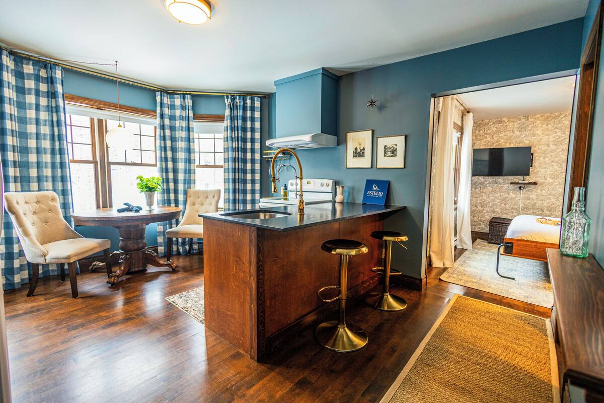 A modern kitchen with a central island, bar stools, and a dining area with chairs.