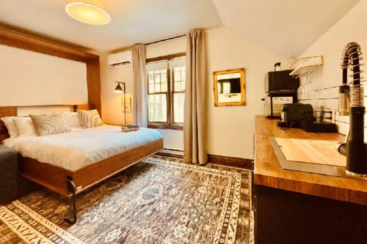 A bedroom with a bed, a desk, a chair, a mirror, and a window.
