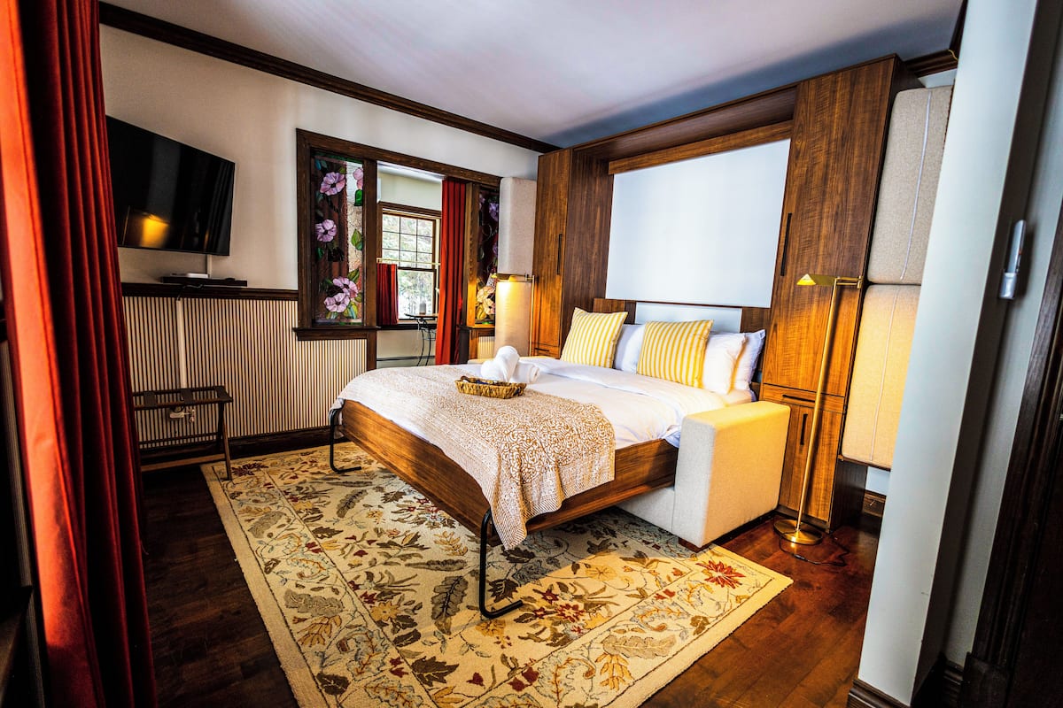 A bedroom with a large bed, bedside lamps, a TV, and a window with curtains.