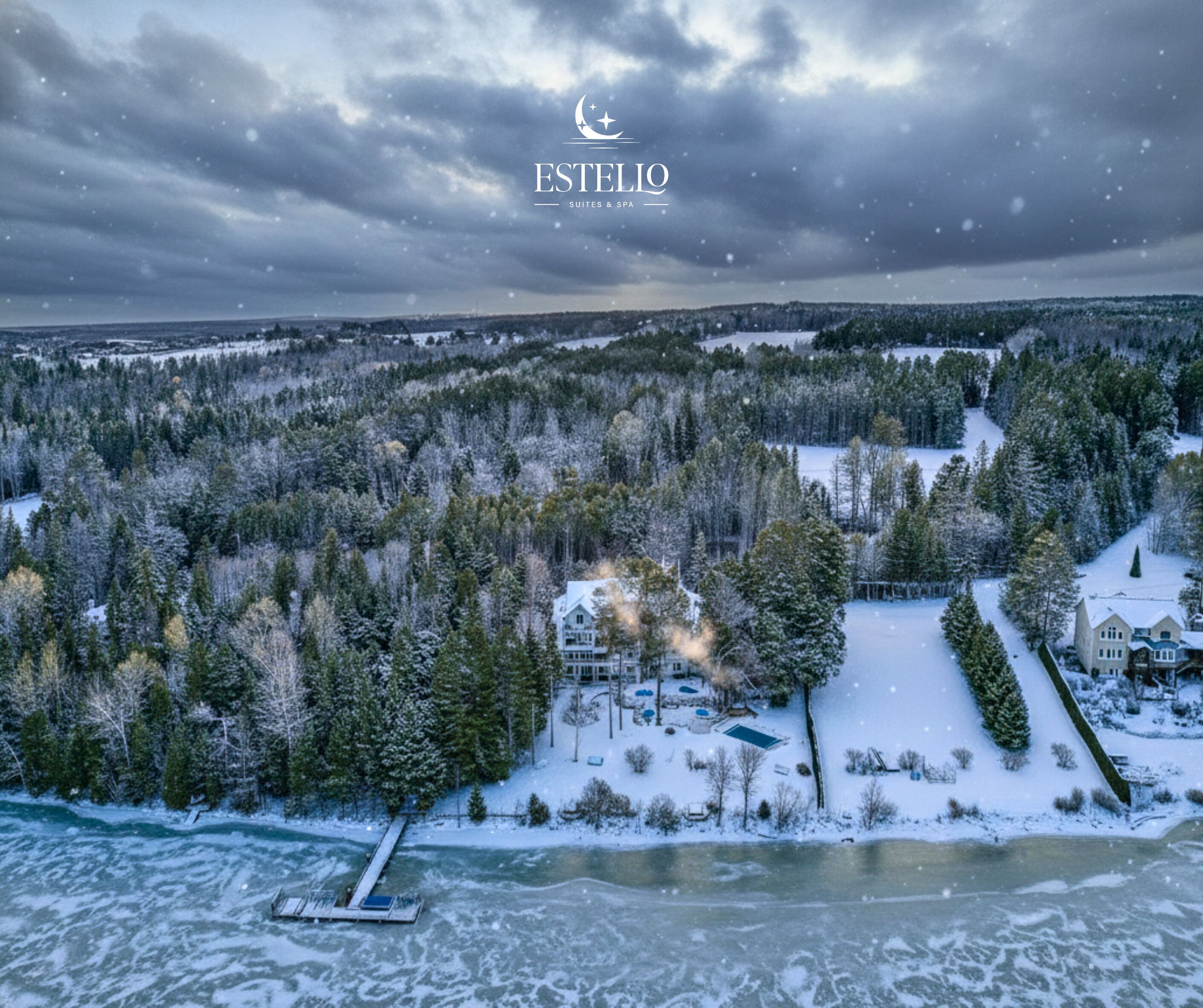 A snow-covered landscape with a large house surrounded by trees, a dock, and a frozen lake.
