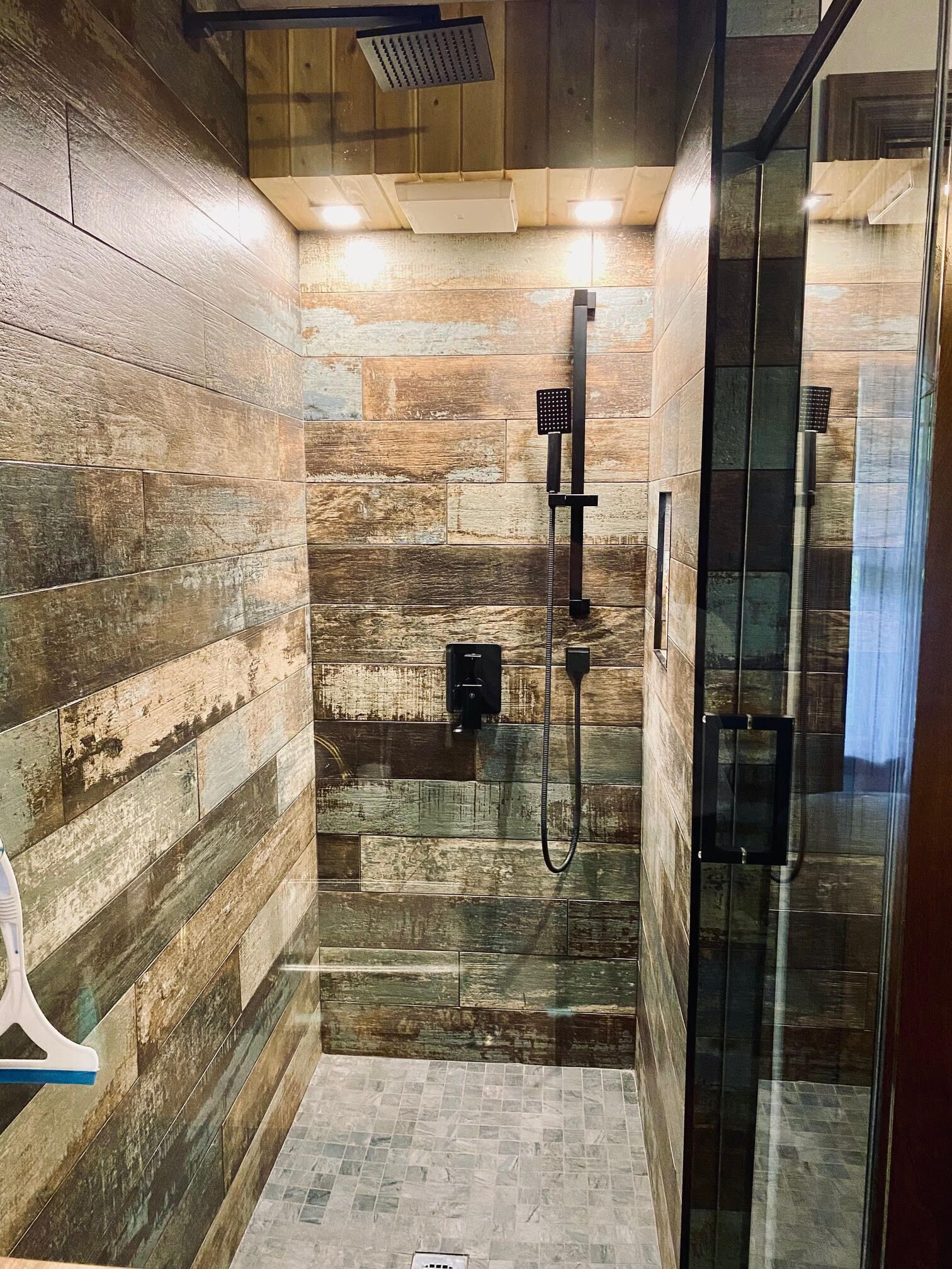 A modern bathroom with wooden wall panels, a glass shower enclosure, and a visible showerhead.