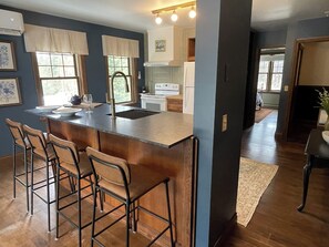 A modern kitchen with a central island, bar stools, and a view into the dining area. - Estello Suites et Spa (Frontenac)
