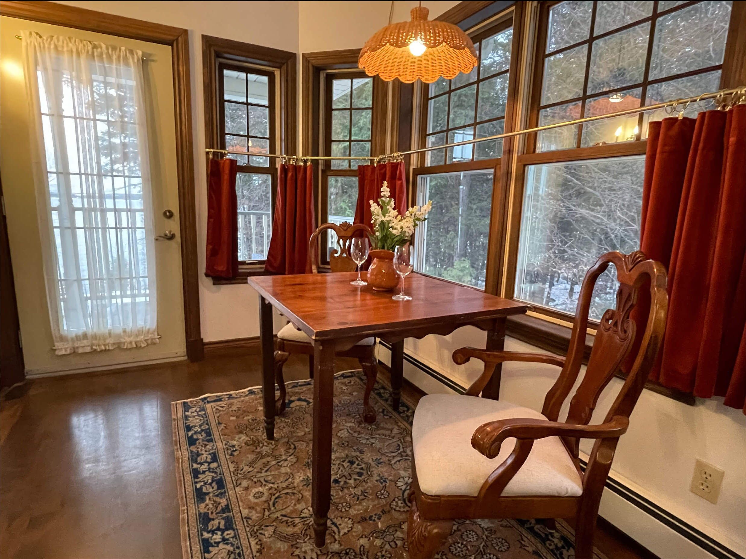 A dining area with a wooden table, chairs, a rug, and a window with curtains.